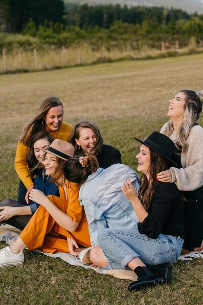 A group of friends laughing on a blanket in the park