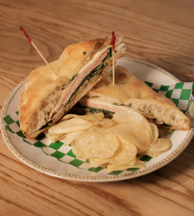 Italian sandwich with deli meat, lettuce, and pesto on artisan bread, served with pickles at Lyla's House in Georgetown, ON.