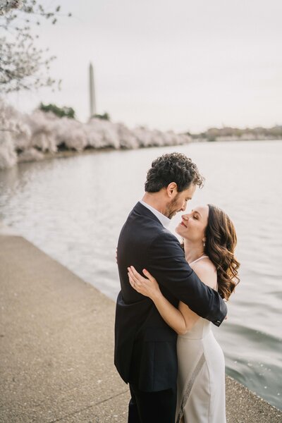 couple half body holding each other by the river in  at cherry blossom with Washington monument in the background