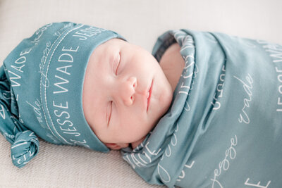 A baby wrapped in a green blanket and matching hat sleeping during his newborn photoshoot in  a studio in Huntsville Alabama