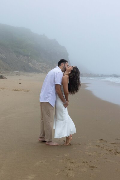 Man kisses his fiancé on the cheek during their engagement session on Block Island.