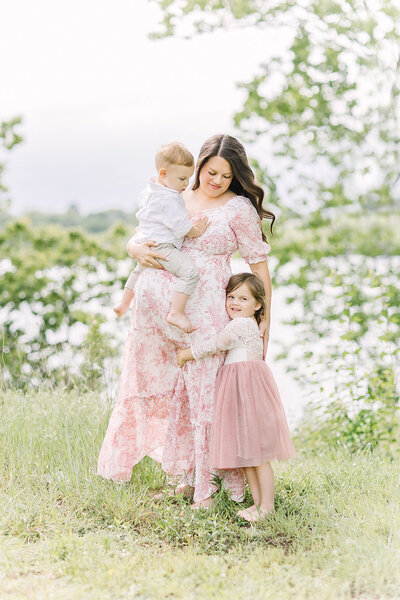 Pregnant mother with her two toddler children in a grassy field next to a lake for her Kansas City maternity photos