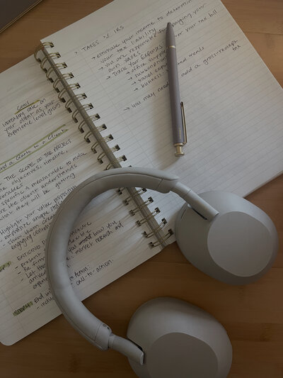 Open notebook with notes inside, pen and headphones on table