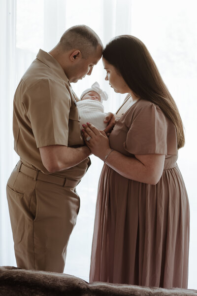 Dad in tan Navy uniform holding newborn baby girl with new mom looking at baby in lifestyle studio in Severn Maryland