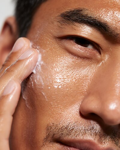close-up of Asian man massaging cream into skin & beard, healthy hydrated look, detailed pores 