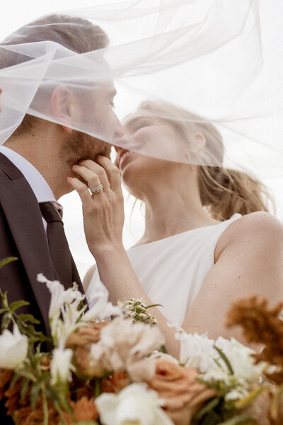 Bride and groom kiss under wedding veil