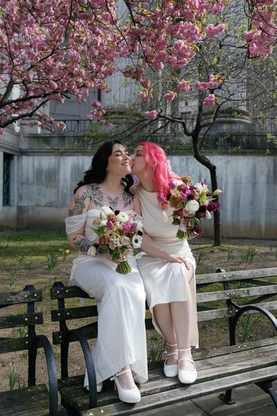 manhattan city hall two brides wearing white dresses pink hair kissing with cherry blossoms and colorful bouquets