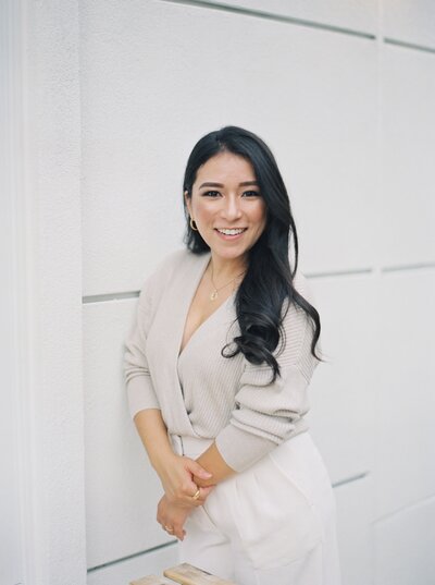 Headshot of Stephanie Michelle, a Dallas wedding photographer, wearing white trousers and a tan sweater