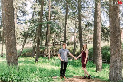 Engaged couple stand in the woods holding hands at the Cedar Grove Park in Tustin