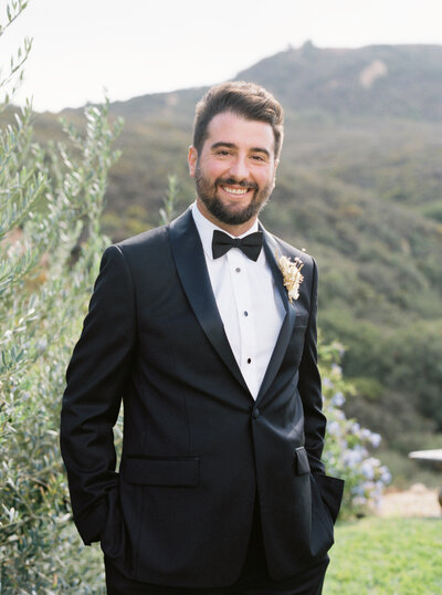 handsome asian groom in tuxedo sitting in a linen club chair