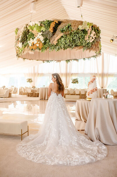 Bride in a lace gown standing under a floral chandelier.