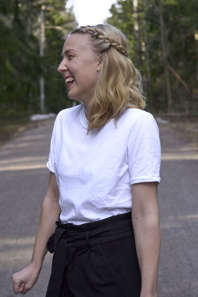 Hyvinvointivalmentaja seisoo metsässä ja hymyilee katsoen sivulle päin