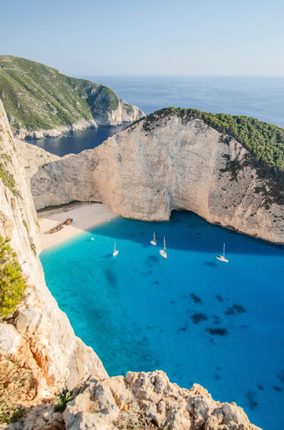 Navagio Beach on Zakynthos, Greece with turquoise water, white cliffs, and sailboats in the bay.