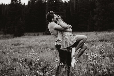Groom lifts bride in a wildflower field during a joyful Breckenridge engagement session.