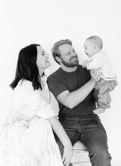 A mother and father smile as the fathers hold up the smiling baby.