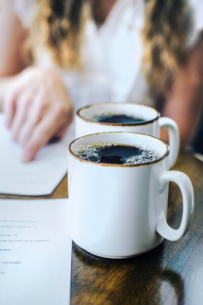 two coffee cups sitting on a table with a woman's hand in the background