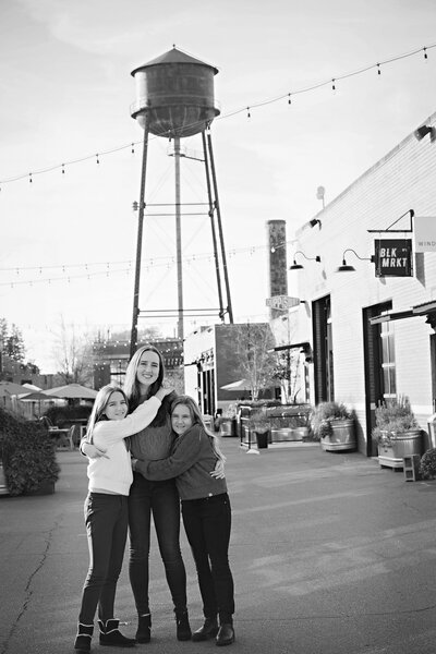 Three sisters in black and white photo posed in front of water tower and brick industrial buildings at Camp North End Charlotte NC