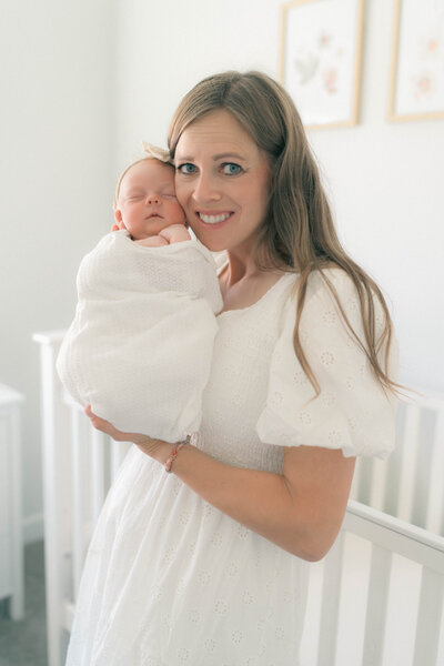 Mother holding swaddled newborn with hands near face during cozy, natural light session by newborn photographer in Utah