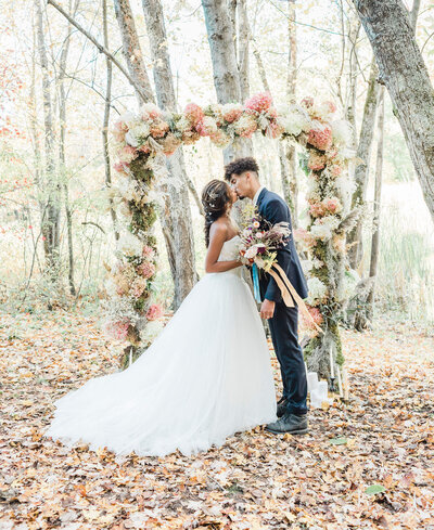 A married couple kissing in front of a floral arch in Ontario.