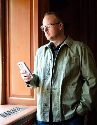 Dr. Mike, shown here standing by a window looking at his phone, recognizes the sensitivity surrounding discussions on sex.