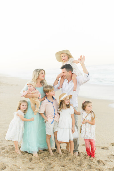 Young family of 6 kids standing and interacting on the beach at sunset