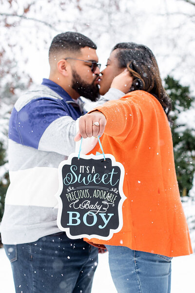 Couple holds sign announcing baby boy in maternity photos