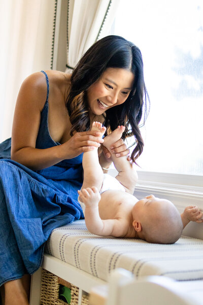 Joyful mom playing with her baby on a window bench during an in-home lifestyle session by a Bay Area family photographer.