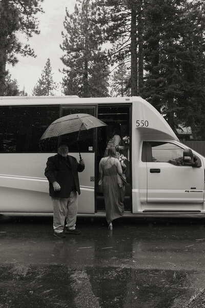 man holding an umbrella for wedding guests in the rain