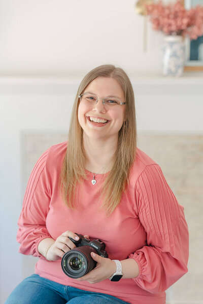 Northern Virginia photographer, Melissa Driggers, sitting at a desk working on her laptop and smiling at the camera.