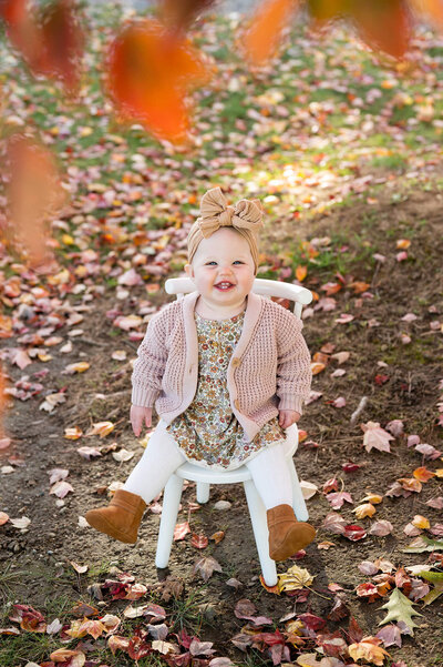 young baby smiling at the camera surrounded by fall foliage