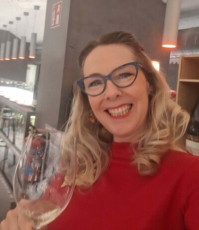 Maria Cristina Barrero smiling and posing for a picture with a glass of white wine in her hand.