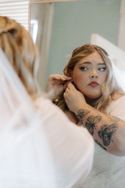 Bride getting ready before her wedding, having her earrings put on while looking in the mirror - photographed by KateLens Photography in North Augusta, SC.