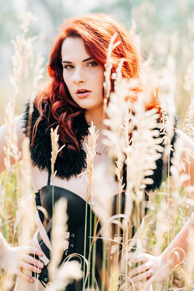 Outdoor boudoir woman in black lingerie kneeling in tall yellow grasses