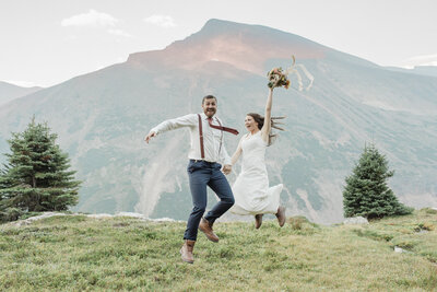 A couple jumps up and down in front of a mountain during their banff national park elopement