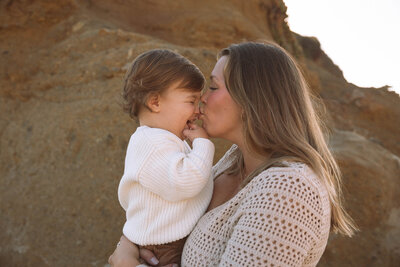 Mother and son sharing a playful kiss during a family photo session at Goff Cove in Laguna Beach, captured by Orange County family photographer Maria Alcantara.