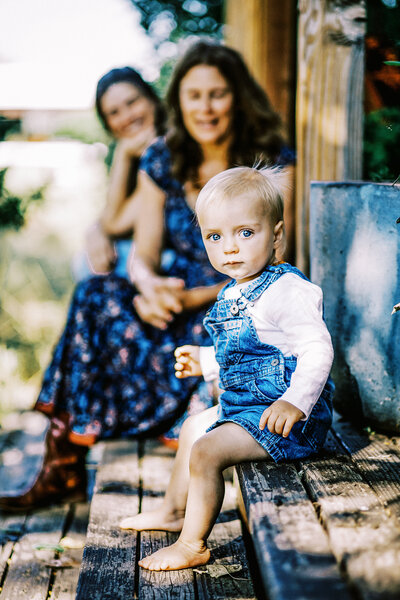 A blonde child with blue eyes sits on a wooden deck
