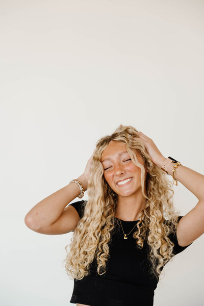 A person smiling and pushing up their hair with their hands