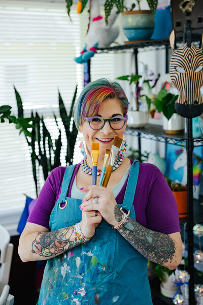 Colorful Artist smiling while holding her paintbrushes