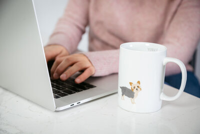 close up of hands typing and a coffee mug with a yorkshire terrier on it