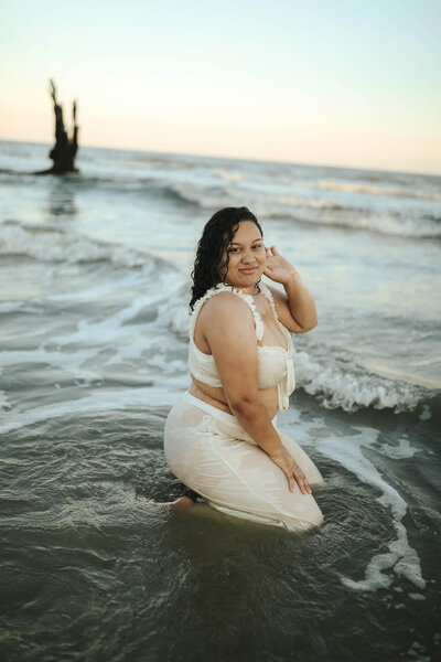 Brunette female sitting in the water on the beach posing for camera