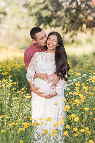 man and pregnant wife in field of yellow flowers