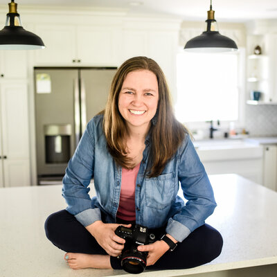 Danielle Hardesty sitting on kitchen counter holding camera and smiling | chicagoland brand photographer for small businesses