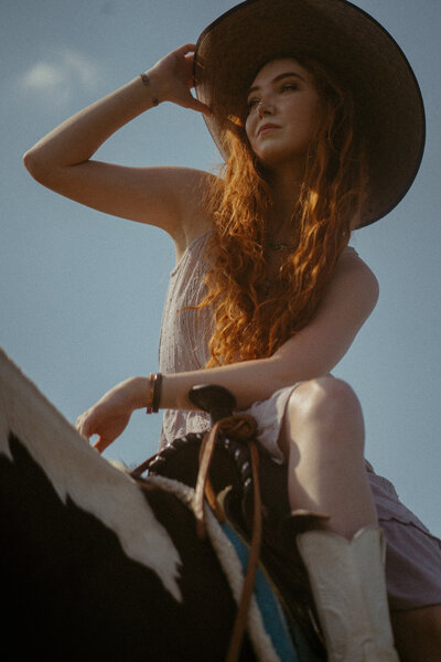 A bride and groom walk through a Tennessee field in thrifted wedding clothes with the setting sun behind them and cowboy hats on.