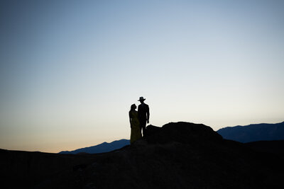 A couple standing hand in hand is silhouetted against a darkening sky