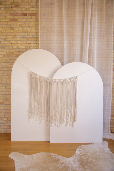 A macrame wall hanging set up on two white wooden arch backdrops.