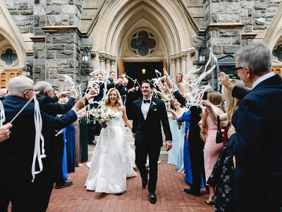 Couple exit their wedding ceremony as guests wave ribbons as they walk out of the church. 