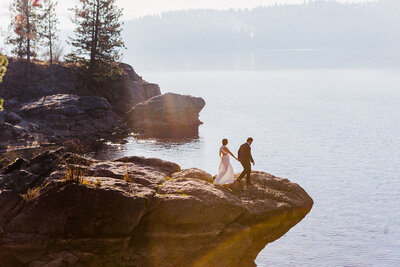 Bride and Groom holding hands standing on rock over Lake Coeur d' Alene