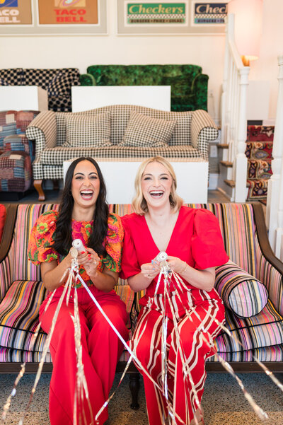 Dr. Brooks and Dr. Templeton, orthodontists in Nashville, TN smiling together in bright red outfits sitting on a striped couch popping streamers