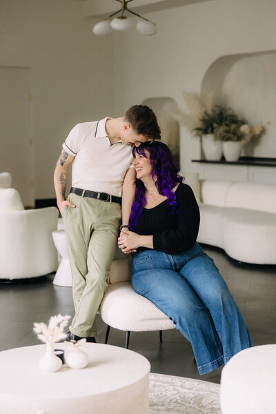 Sara sits on stool with Marc looking down at her, Finger Lakes wedding photographer & videographer