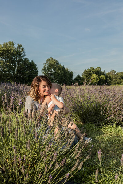 mother cuddles with son and smiles while sitting in lavender field at lavender lane in milan michigan